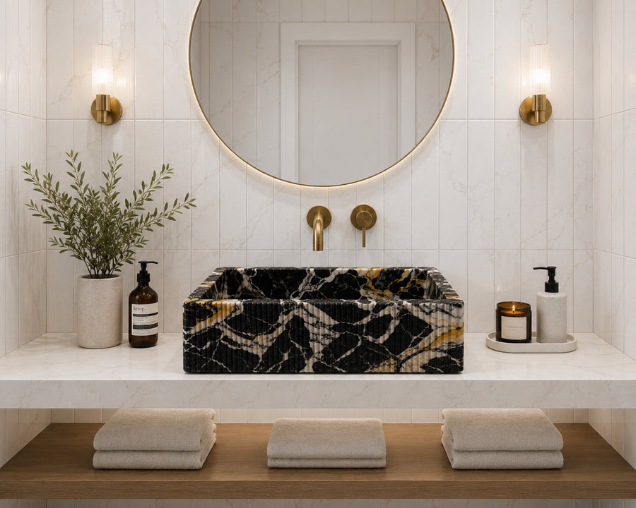 Premium front view of a handmade black marble vessel sink showcased in a bright contemporary bathroom with white marble-look tiled walls, brushed brass faucet, floating vanity, and soft natural lighting, highlighting the stone's rich texture and craftsman